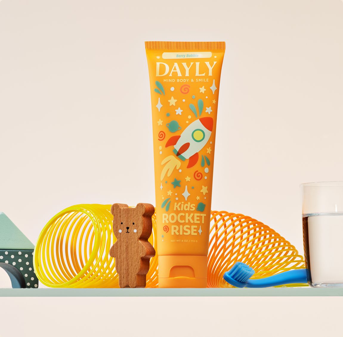 DAYLY ROCKET RISE kids toothpaste on a bathroom shelf with a toy slinky and teddy bear