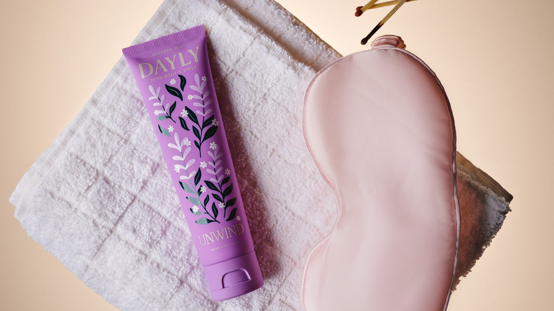 DAYLY Unwind toothpaste on a towel next to a silk sleep mask and candle